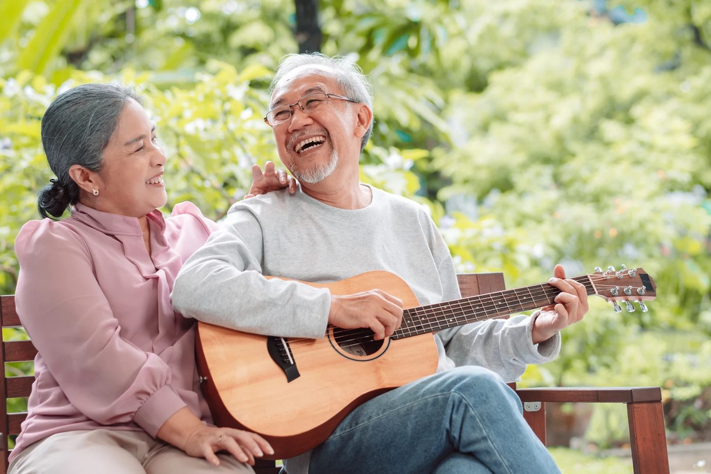 Older couple smiling together on a garden bench while one plays guitar, reflecting senior years mental health, joy, and connection.