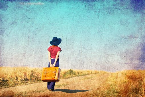 Rear view girl with suitcase on countryside road
