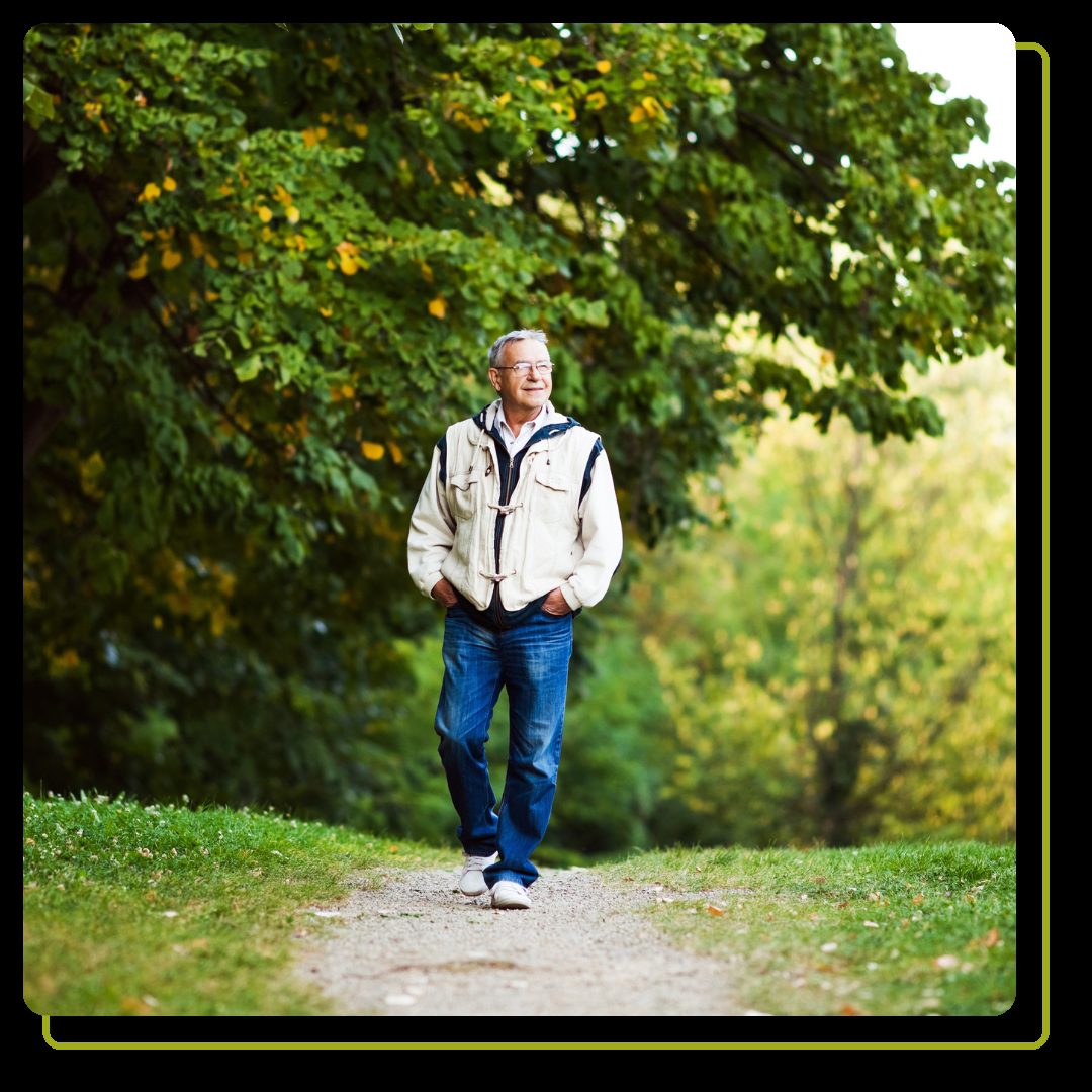 middle aged man walking on dirt trail with trees behind him