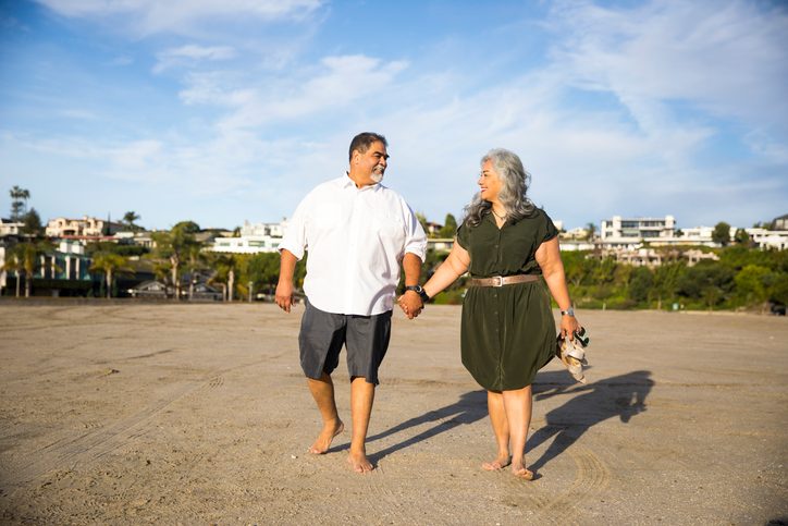 Couple walks along beach, holding hands.