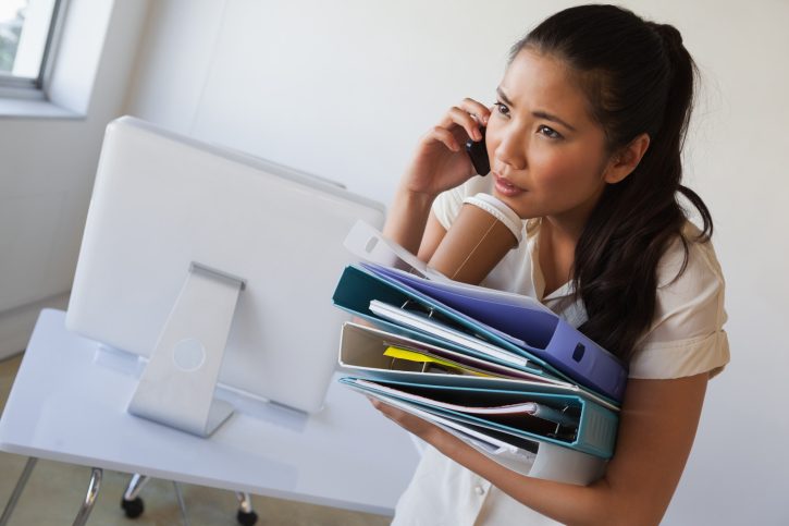 Casual businesswoman balancing coffee on pile of folders