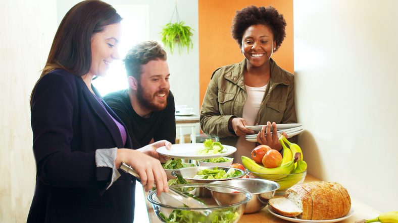 Group of three close friends (adults in their thirties) prepare food around kitchen island