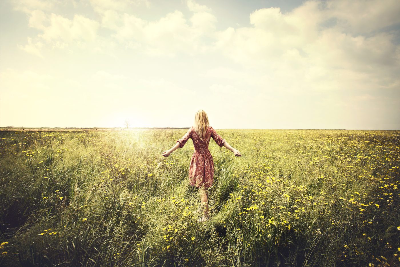 Woman walking through field toward the sun