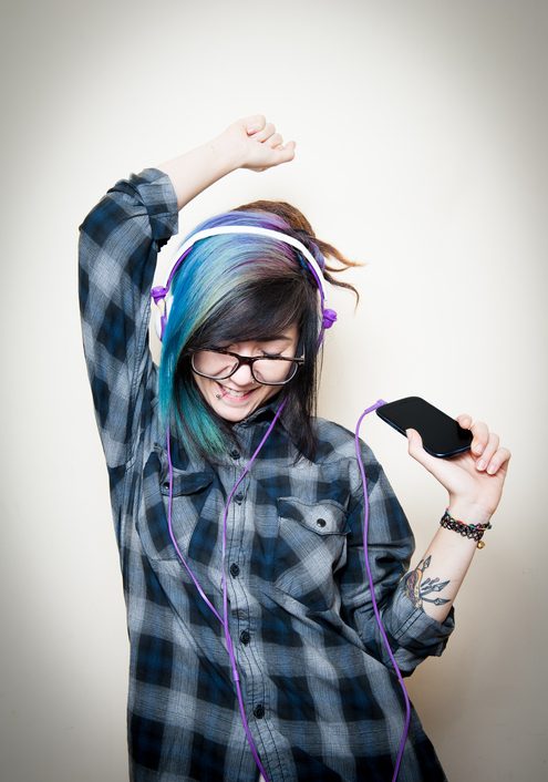 Young adult with headphones and brightly dyed hair listens to music