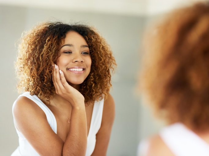 Person with natural hair looks into mirror smiling widely