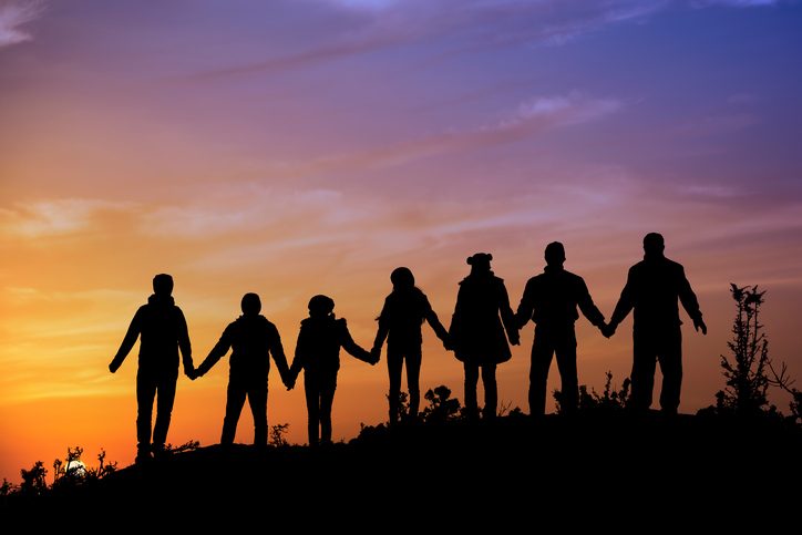 Rear view of seven people holding hands on hill, gazing at purple and orange sunset