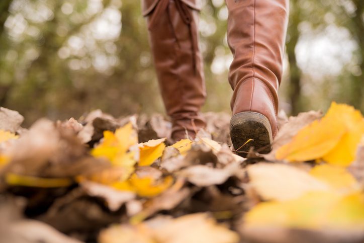 Close-up photo of booted feet walking through leaves