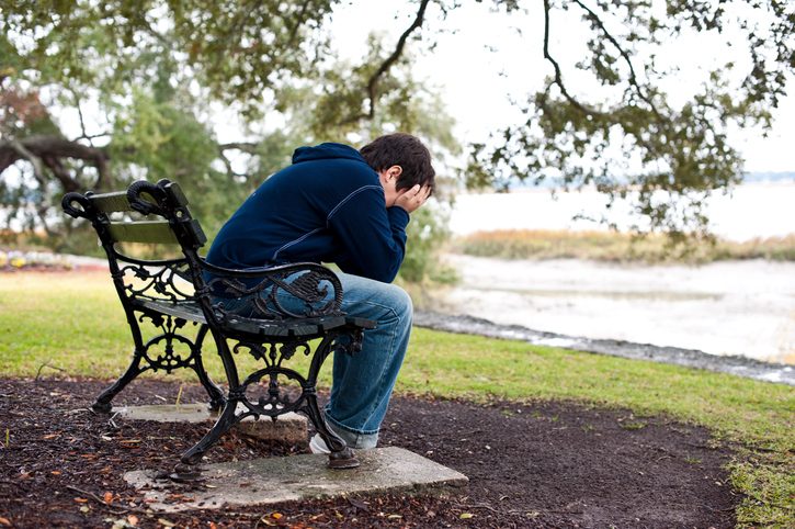 Child in jeans and hoodie sits on bench with head in hands