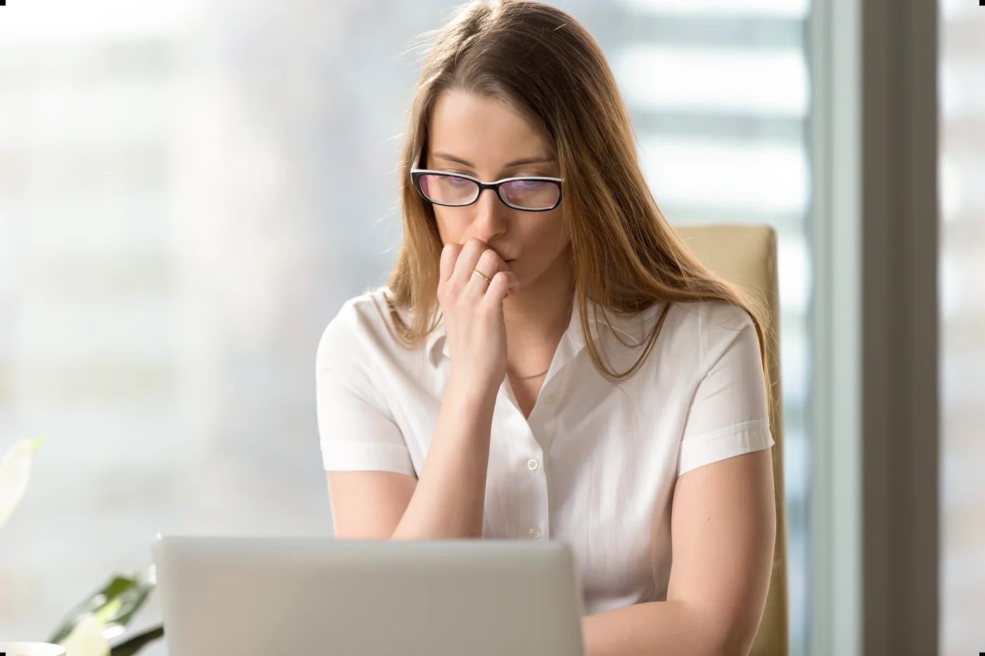 A professional looks uncertain while working at a laptop, reflecting self-doubt associated with imposter syndrome.