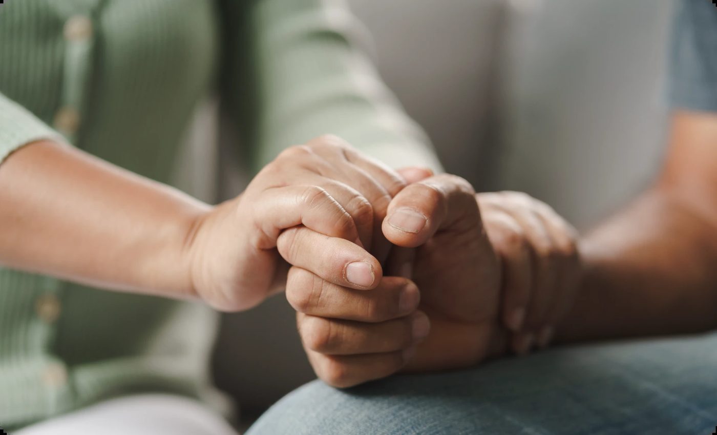 Close-up of a therapist gently holding a client's clasped hands during a supportive types of therapy session, showing empathy and connection