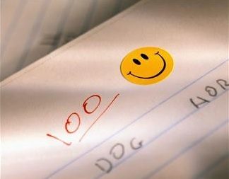 A grade-school paper shoes 100% grade marked on it, and has a smiley-face sticker added/