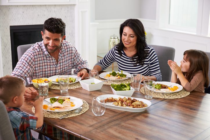 Two parents and two children sit down at the table to enjoy a meal together, talking and smiling