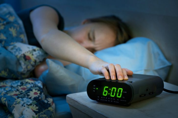 Teenage girl pressing snooze on her alarm in the morning