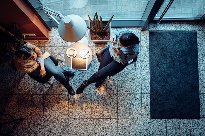 Overhead view of two friends talking in a coffee shop.