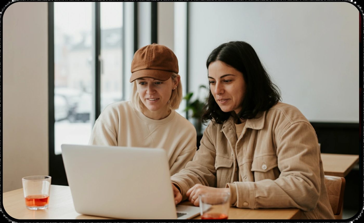Two women working on laptop, showing people pleasing behavior in professional settings.