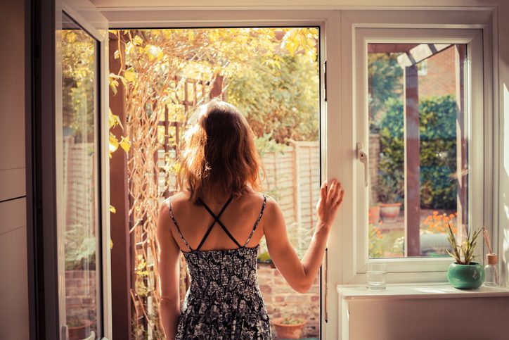 Rear view of person with long hair in tank top standing in open doorway and looking outside
