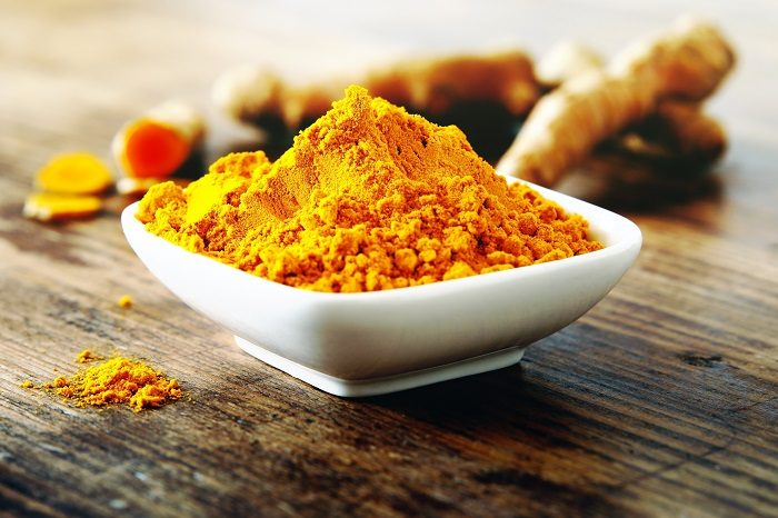 Bowl of turmeric powder with roots in background