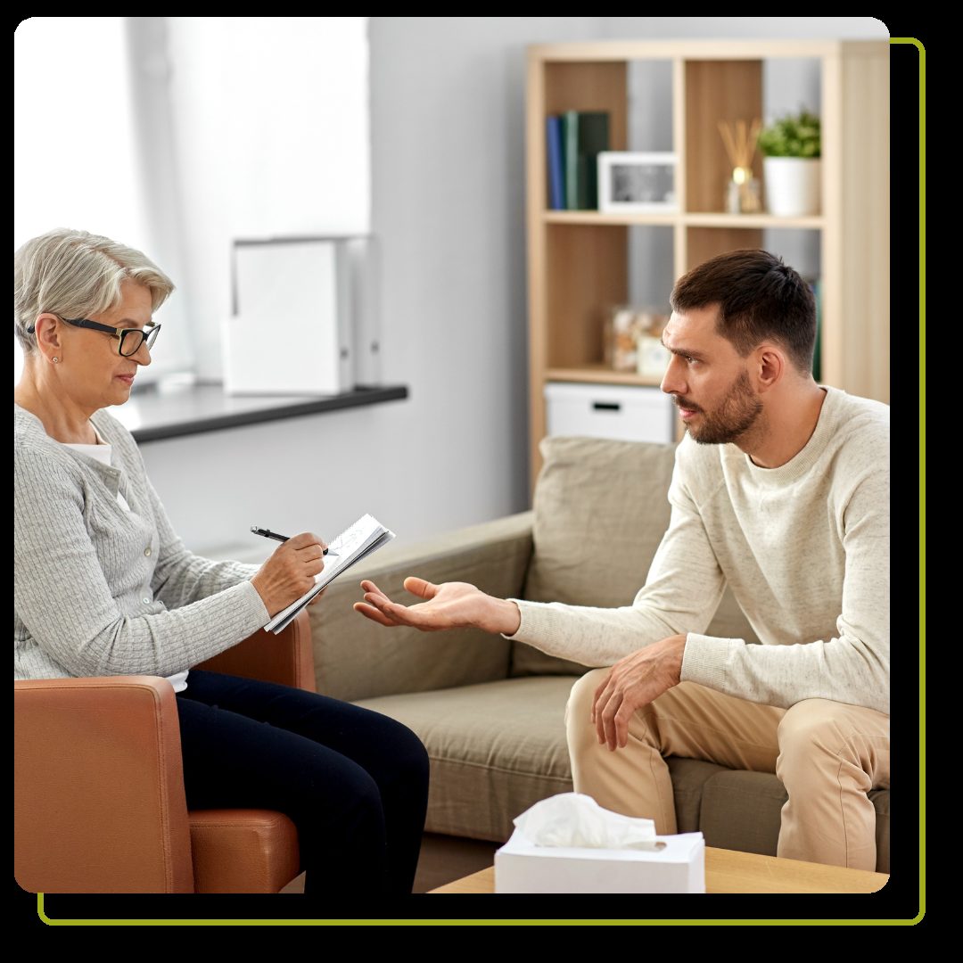 woman psychologist taking notes to notebook and sad young man patient at psychotherapy session