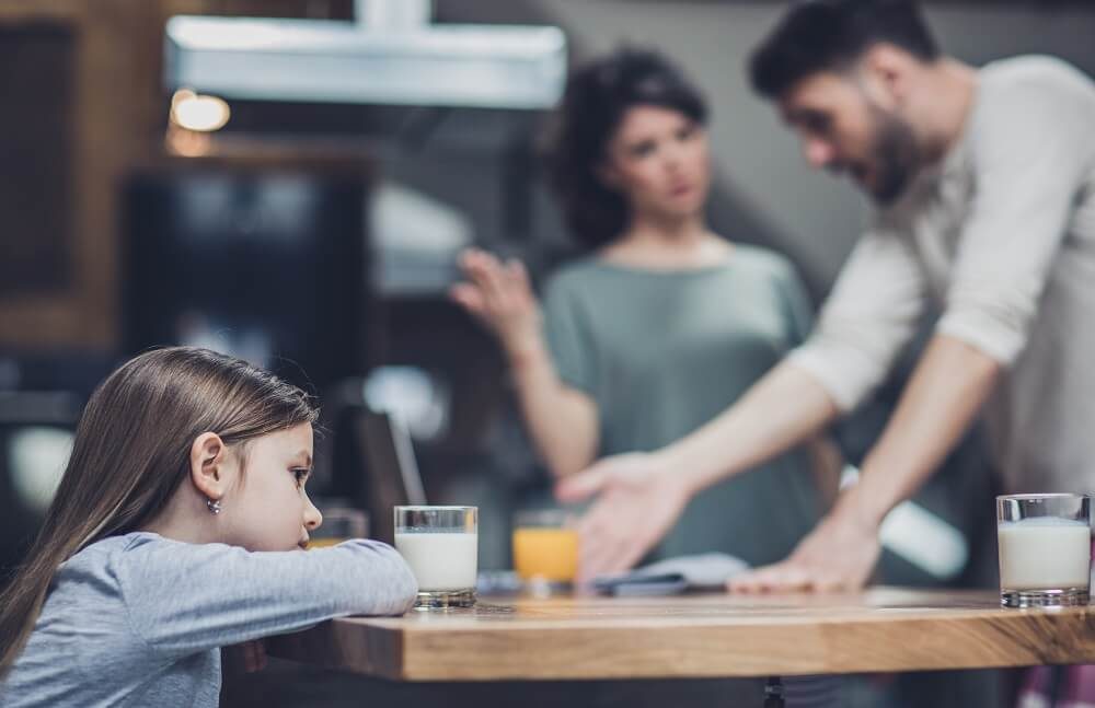 Parents arguing while sad daughter sits at the table