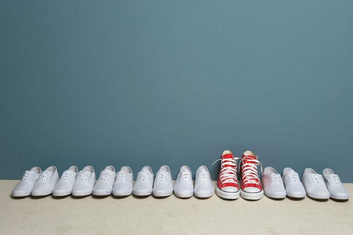 One pair of red shoes stands out in row of white shoes along wall