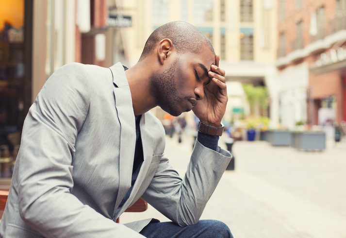 Man in business wear sits on bench, holding his head