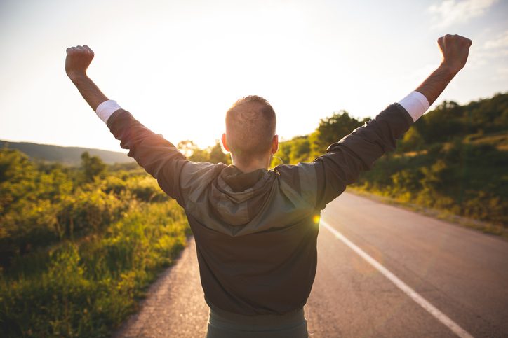 Rear view of person on road raising arms to the sky