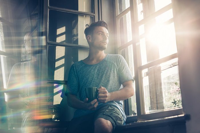 Man sitting on windowsill with cup of tea, looking out window
