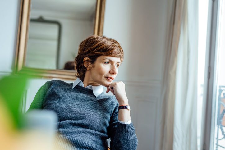 Thoughtful professional wearing sweater with short hair sits in comfortable office looking out window