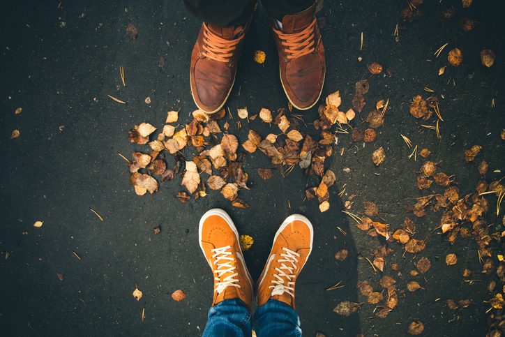 View of the feet in outdoor shoes of two people on ground with leaves. The feet are facing but standing apart