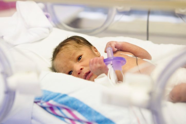 Preterm baby with eyes open lying in incubator