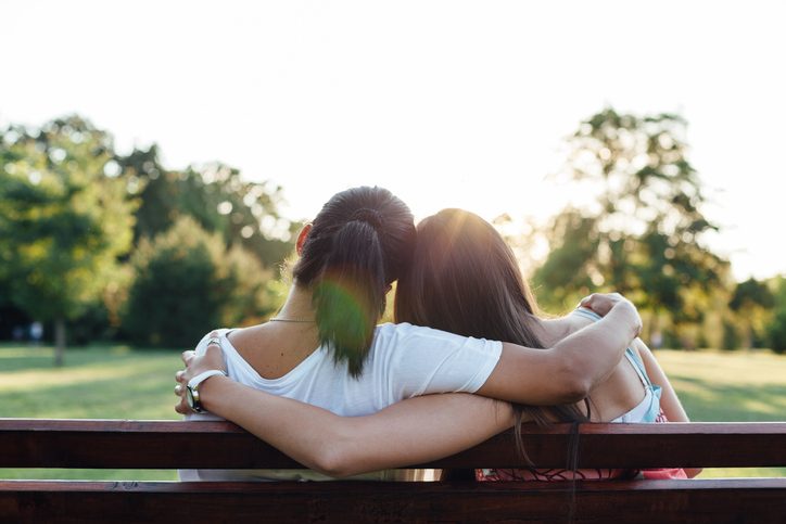 Closeup rear view photo of teen and parent with ponytail sitting on park bench