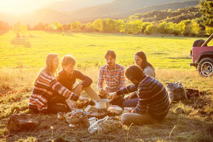 Group of friends sitting out in field camping, talking together