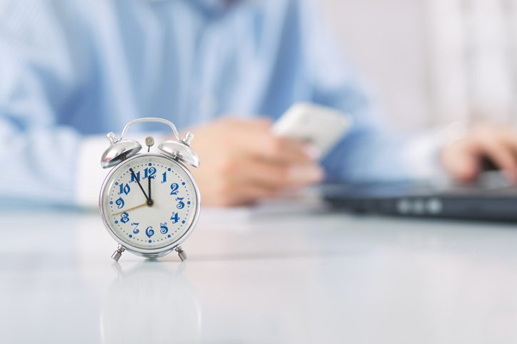 Person works at business desk with alarm clock in sharp focus in foreground