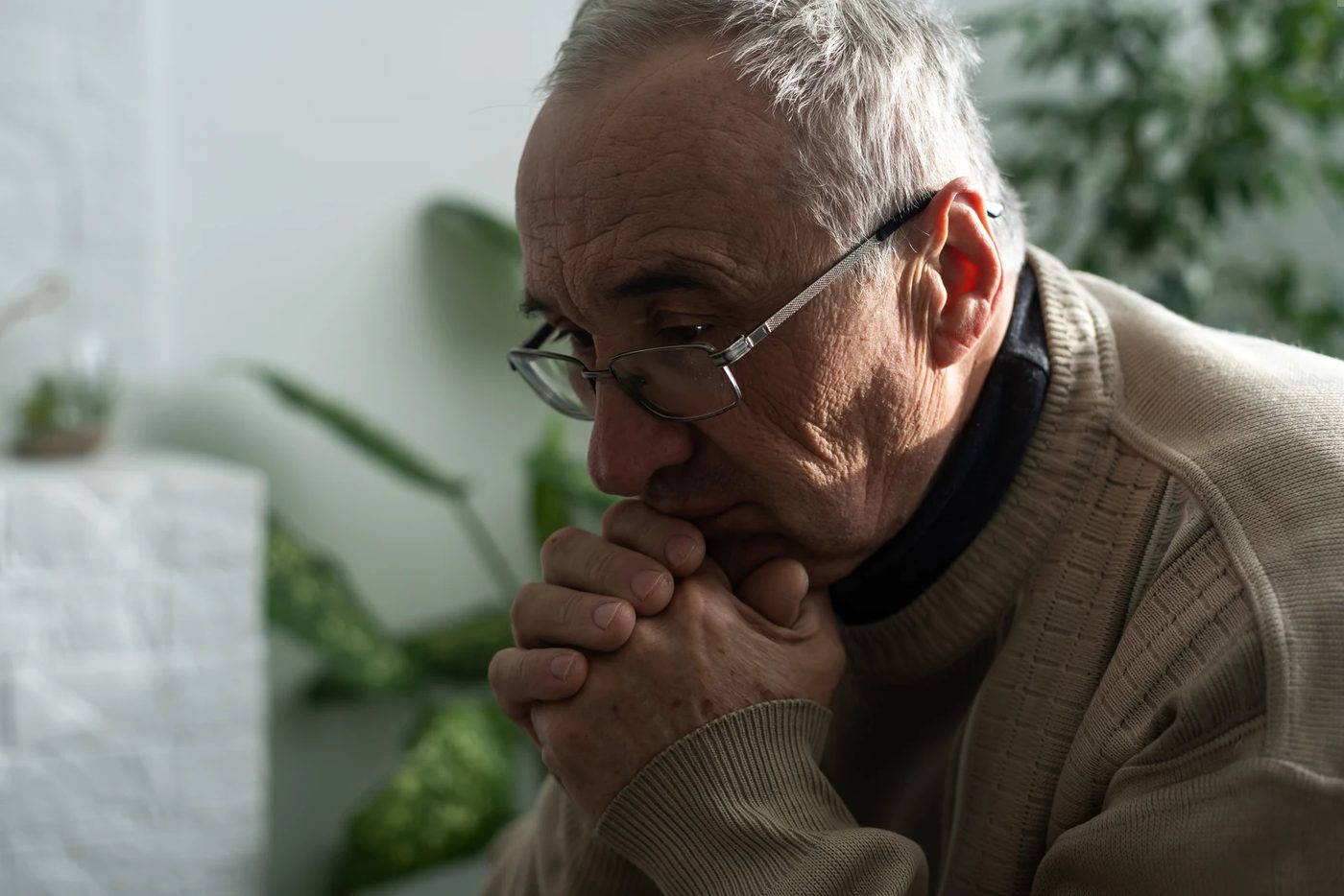 Older man sitting in quiet reflection with hands folded, representing senior years mental health, prayer, stress, and life review.