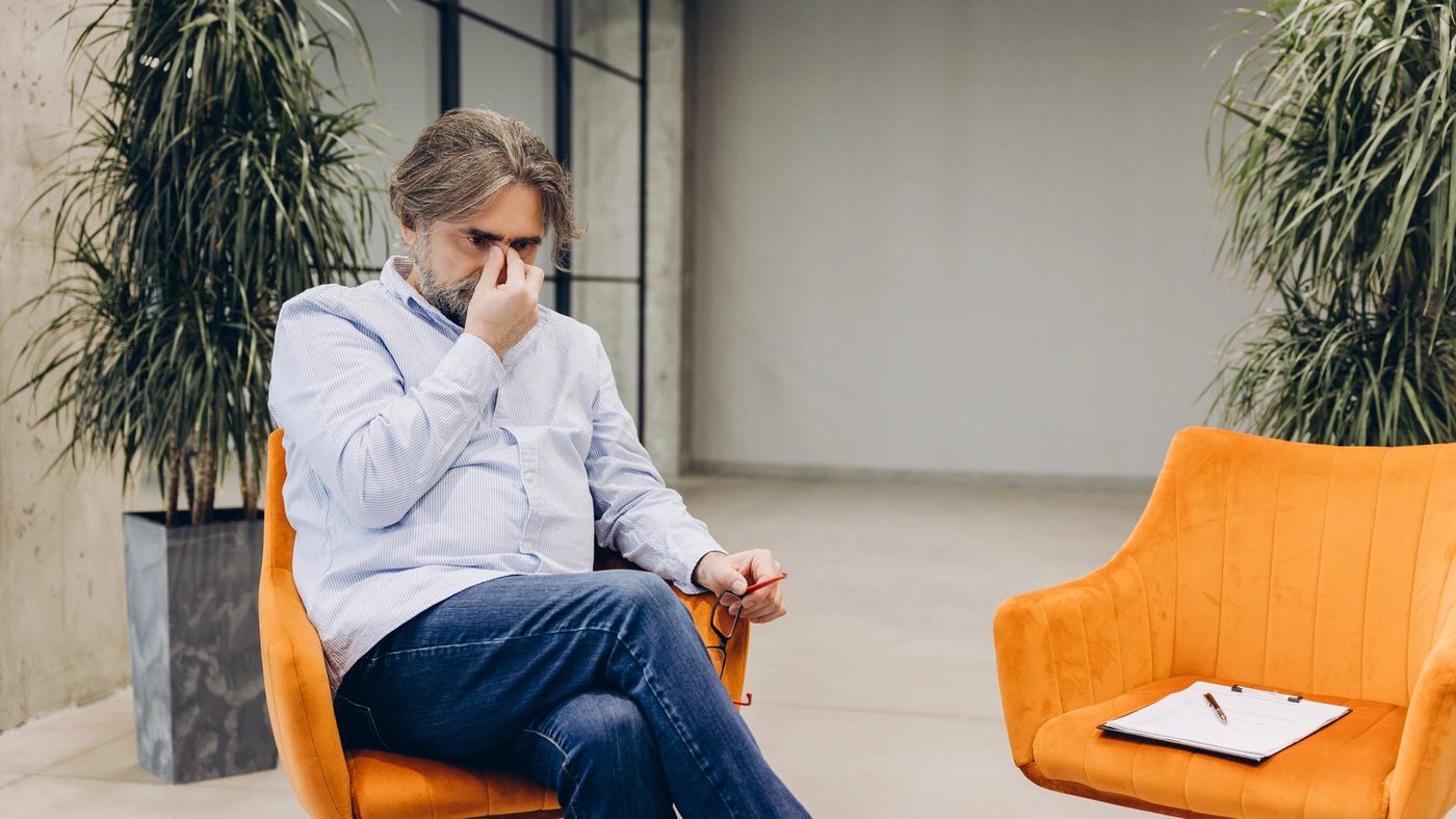 Person sitting in a therapy office chair and rubbing his eyes from stress