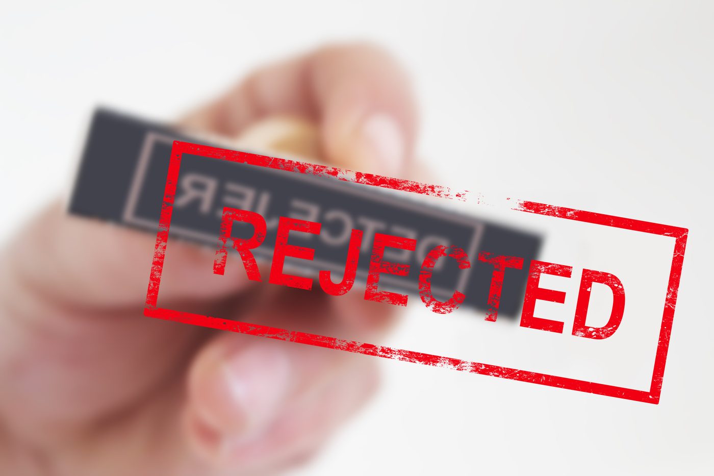 Hand presses a "rejected" stamp onto glass.