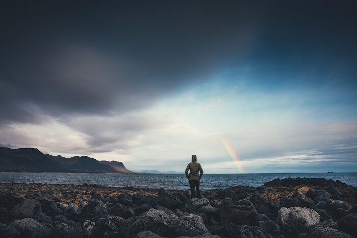 Person watching a rainbow in a cloudy sky