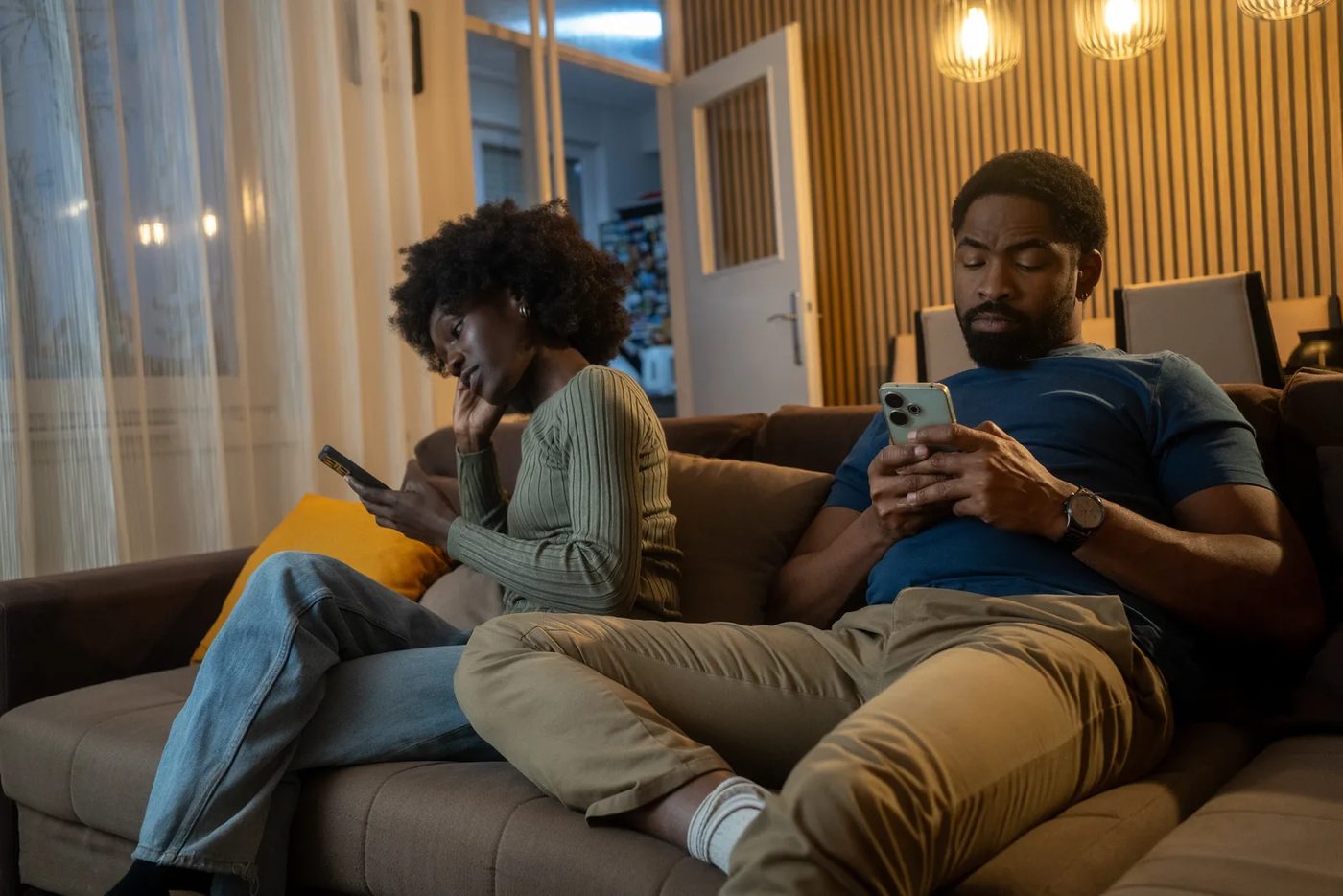 A couple sits quietly after a tense conversation, each holding a phone.