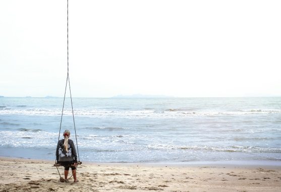 Woman sitting on beach swing facing the sea