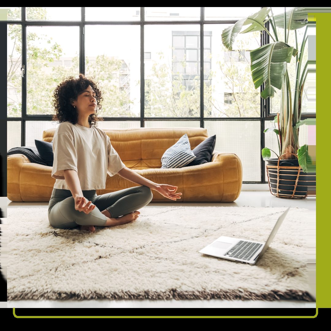 Young woman meditating at home with online video meditation lesson using laptop.
