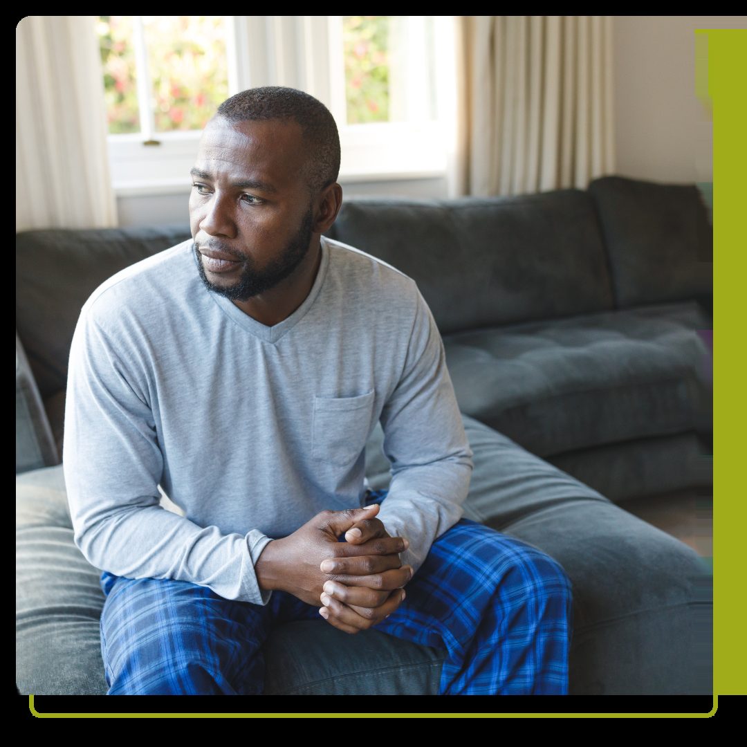 Worried man thinking, sitting on couch looking out of window in living room