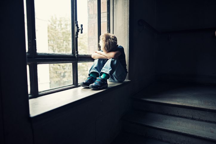 Young child sitting alone in window with head down