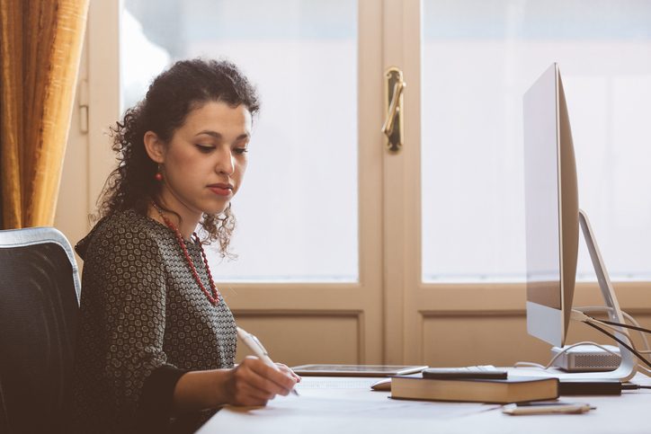 Working at desk with computer and papers, side view