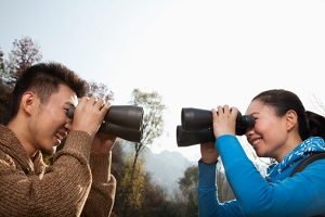 Young Asian couple in a forest smiling and looking at each other through binoculars
