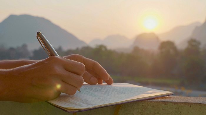 Closeup of hand writing in a journal in a pretty outdoor setting at sunrise