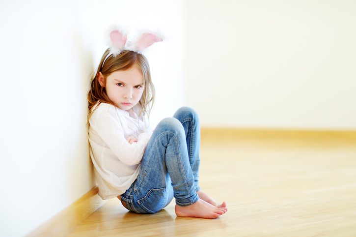 angry child with long hair and rabbit ear costume sits on floor with arms crossed, glaring