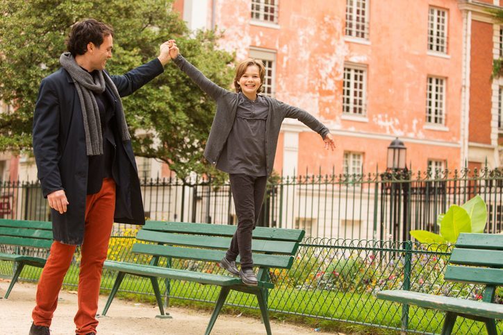 Parent helps grinning child walking on park benches balance