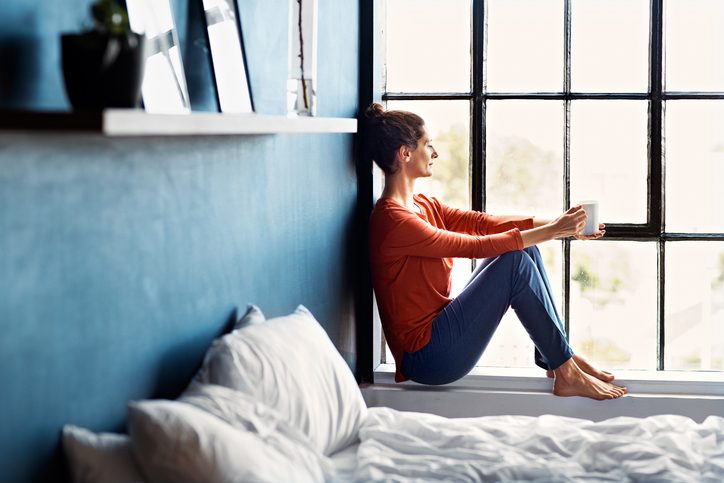 Adult with hair pulled back sits by window peacefully in room