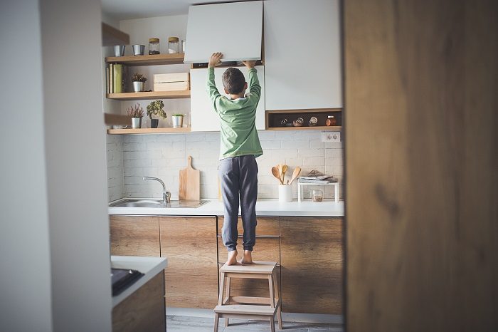 Young boy standing on step stool to steal cookies form kitchen cupboard