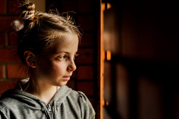 young child with hair up in pigtails looks off to the side in dimly lit room with a serious expression